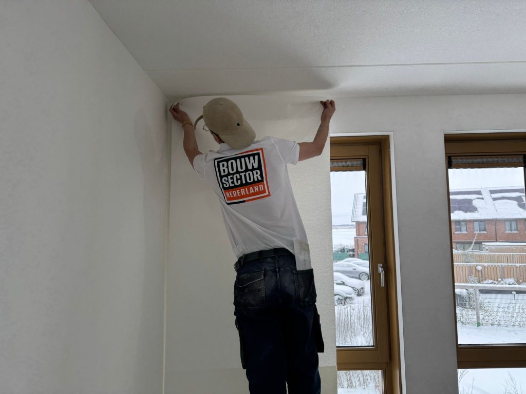 Behanger van Bouwsector Nederland zet een baan tegen het plafond aan in een lichte kamer met houten kozijnen