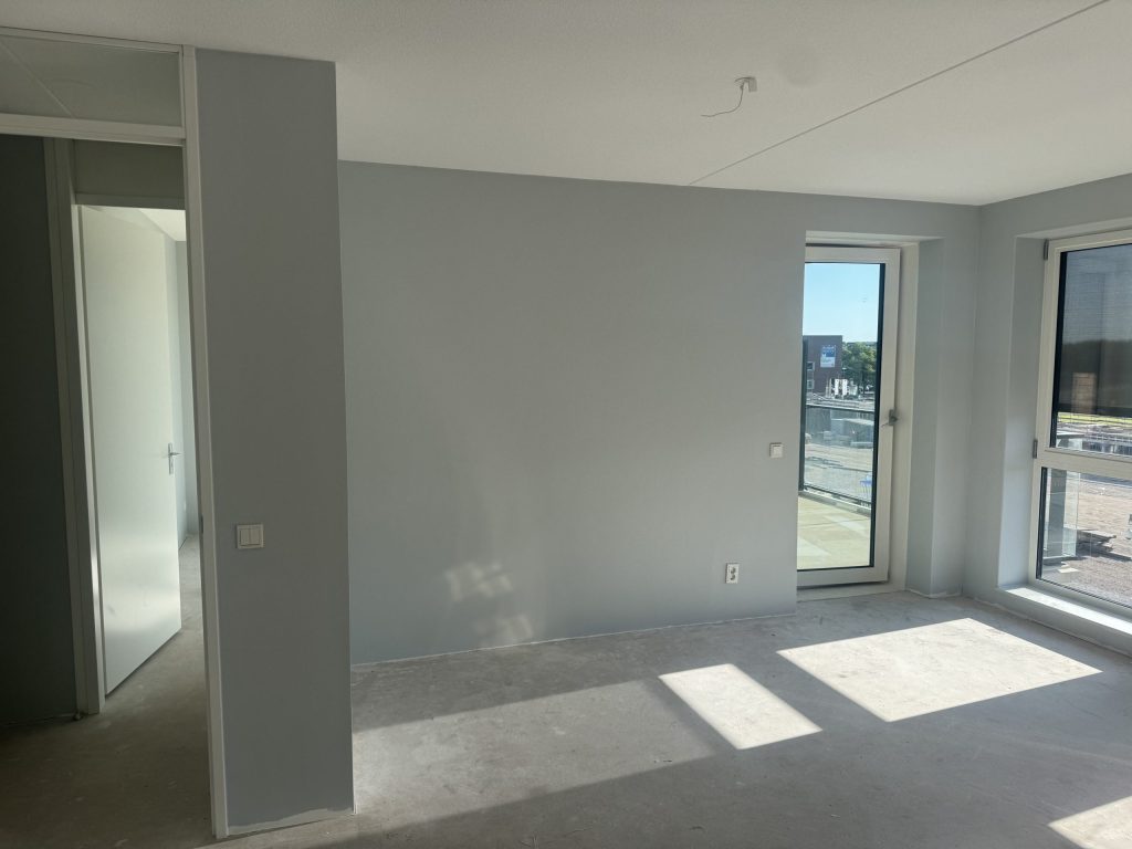 Nieuw appartement met lichtgrijze wanden, een balkondeur en zon op de betonvloer