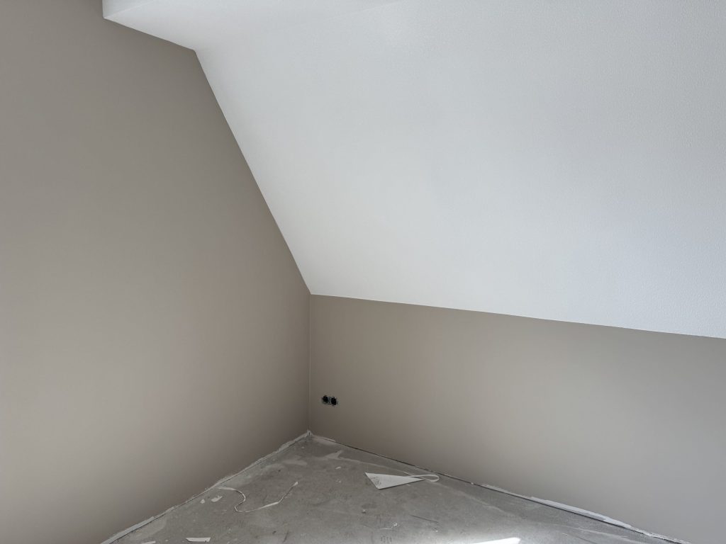 Zolderkamer met schuine wand, lichte muren en een kale betonvloer na het afwerken