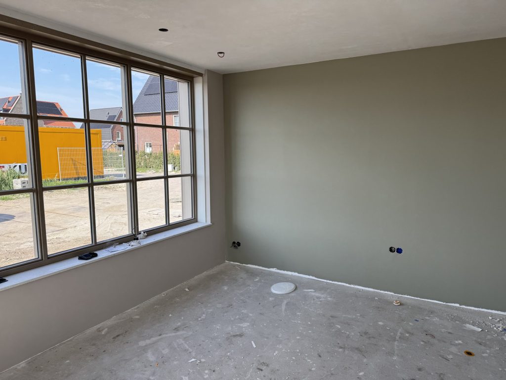 Nieuwbouwkamer met groengrijze wand en een groot raam met uitzicht op de bouwplaats