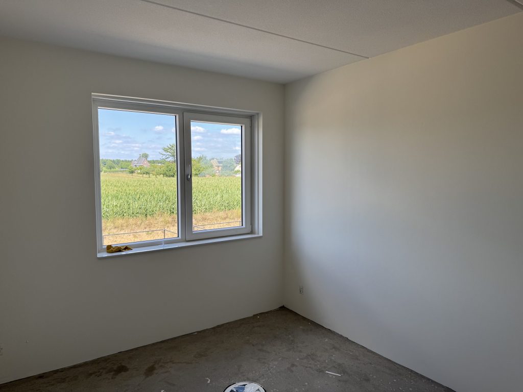 Lege slaapkamer met lichte wanden en een raam dat uitkijkt op een maisveld