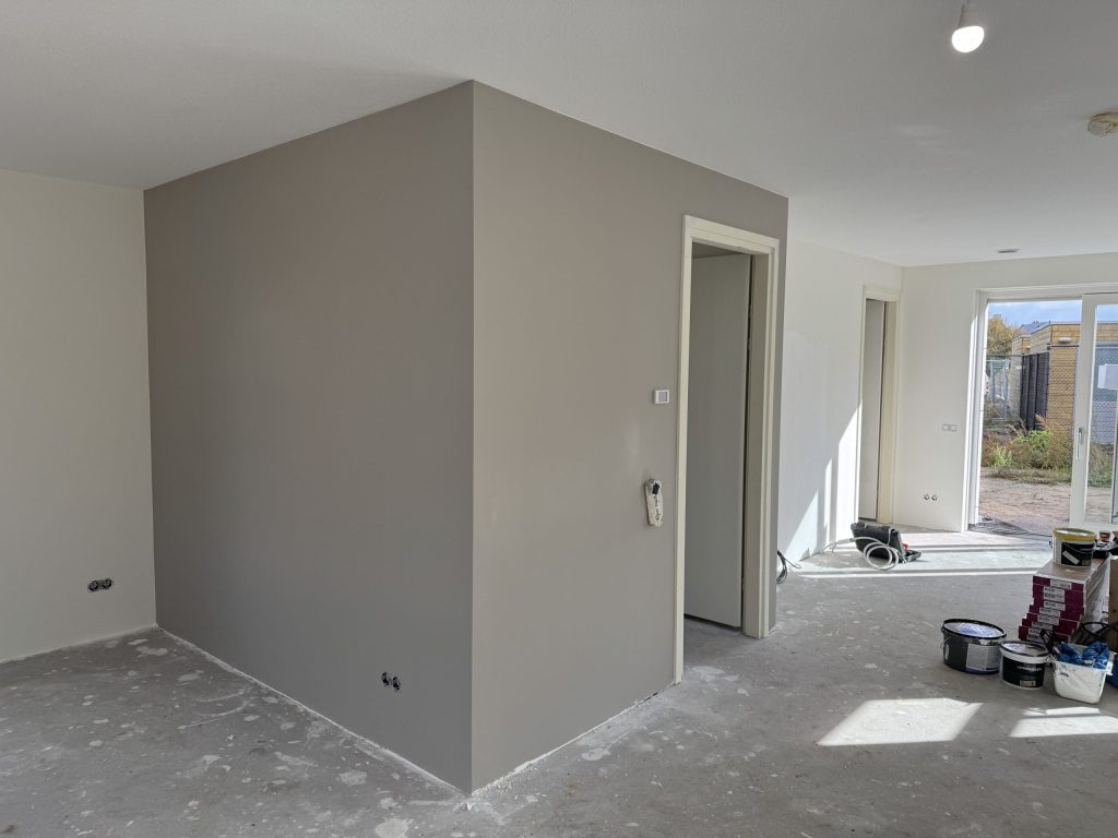 Open woonruimte met een grijze wand rond een deurkozijn en verfemmers bij de tuindeuren
