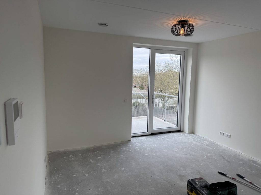 Appartementkamer met witte wanden, een balkondeur en een designlamp aan het plafond