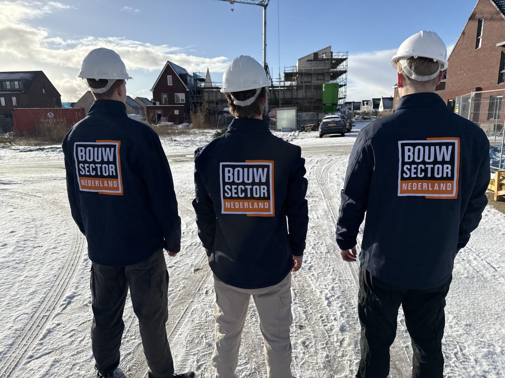 Drie vakmensen in jassen van Bouwsector Nederland met witte helm op een besneeuwde nieuwbouwlocatie